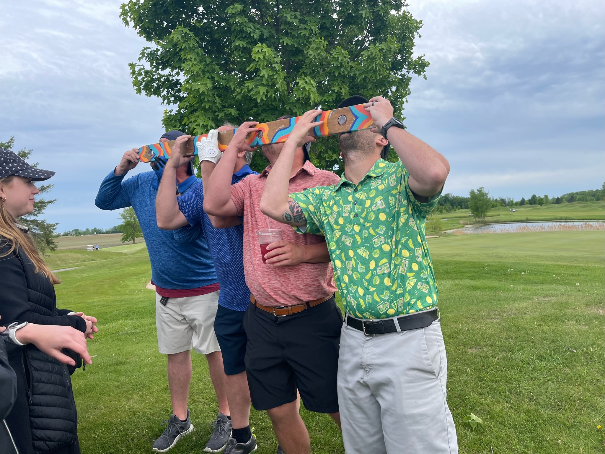 The guys drinking shots together from a long wooden shot board on the golf course