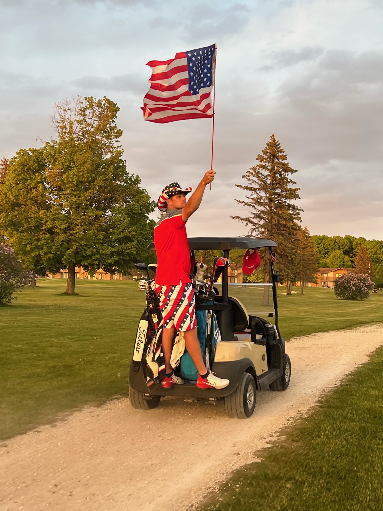 Jake standing on a golf cart holding the American flag after Team Jake won the Ryder Cup playoff