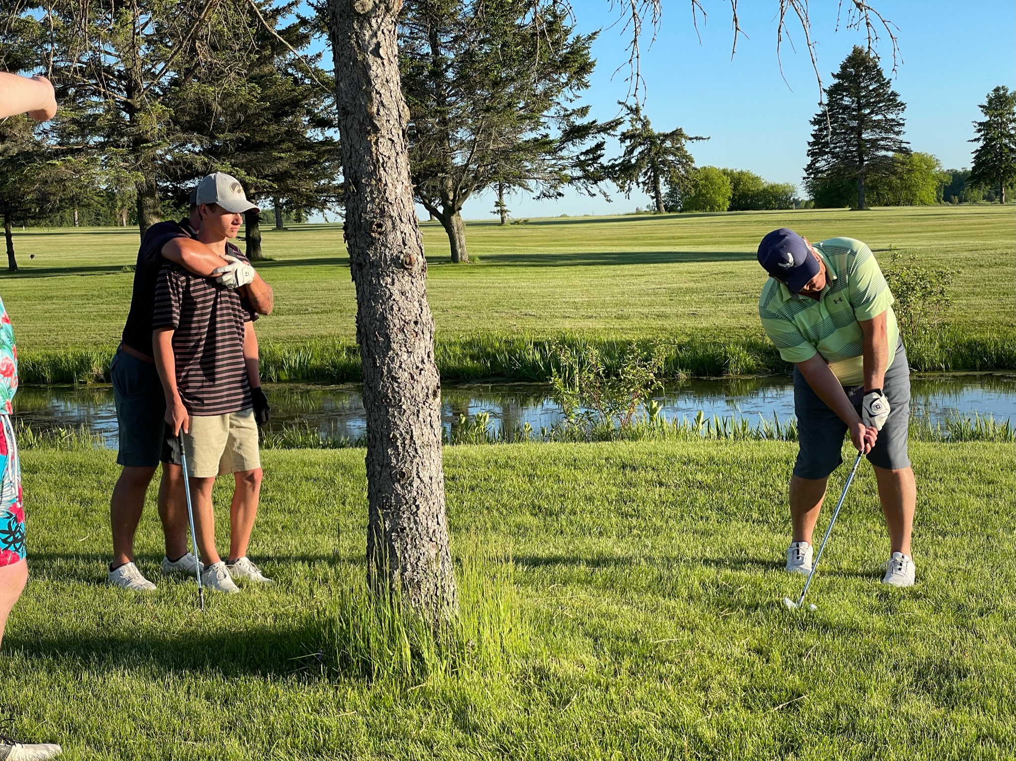 Dean Johnson playing a playoff approach beside the water with Eli Schaefer and Johnny Mack watching